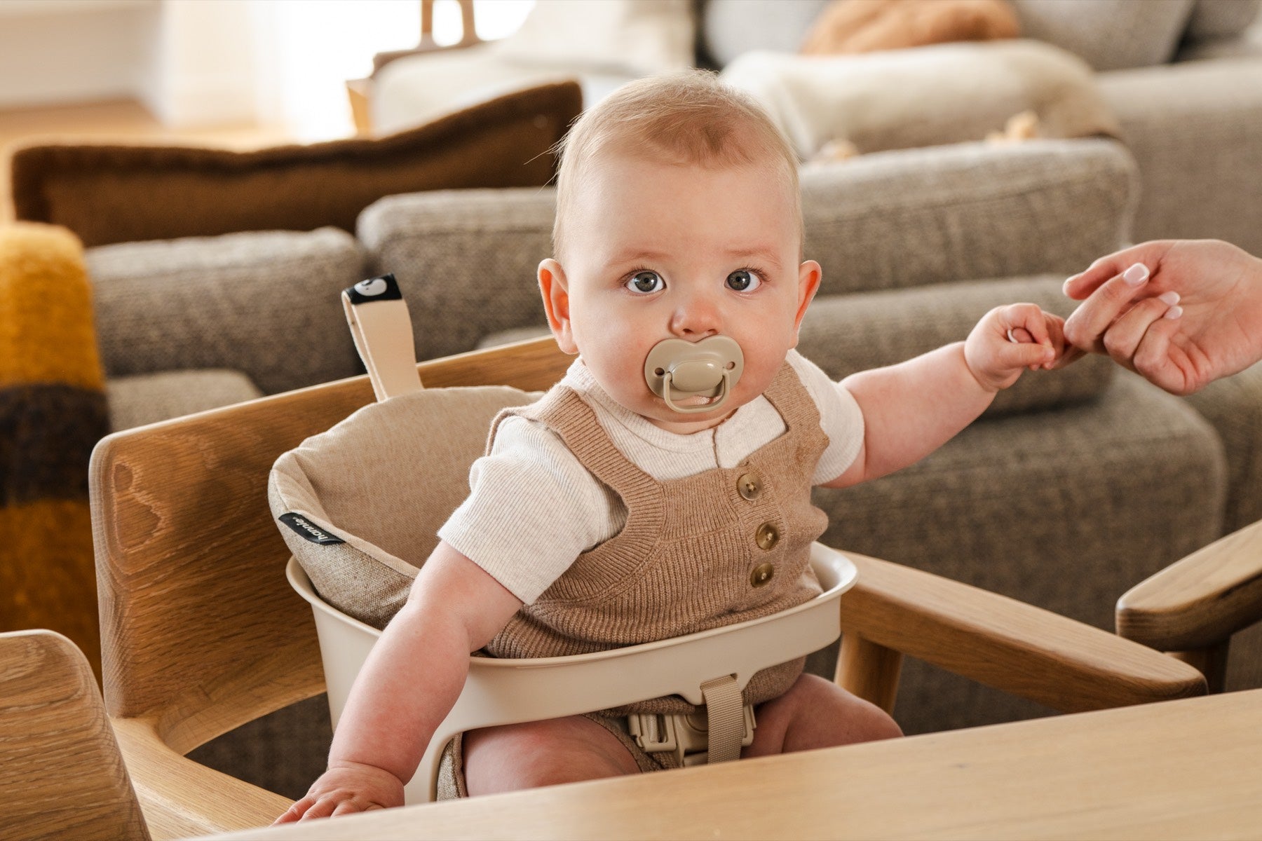 Baby in the Hannie Portable High Chair holding a parent's finger