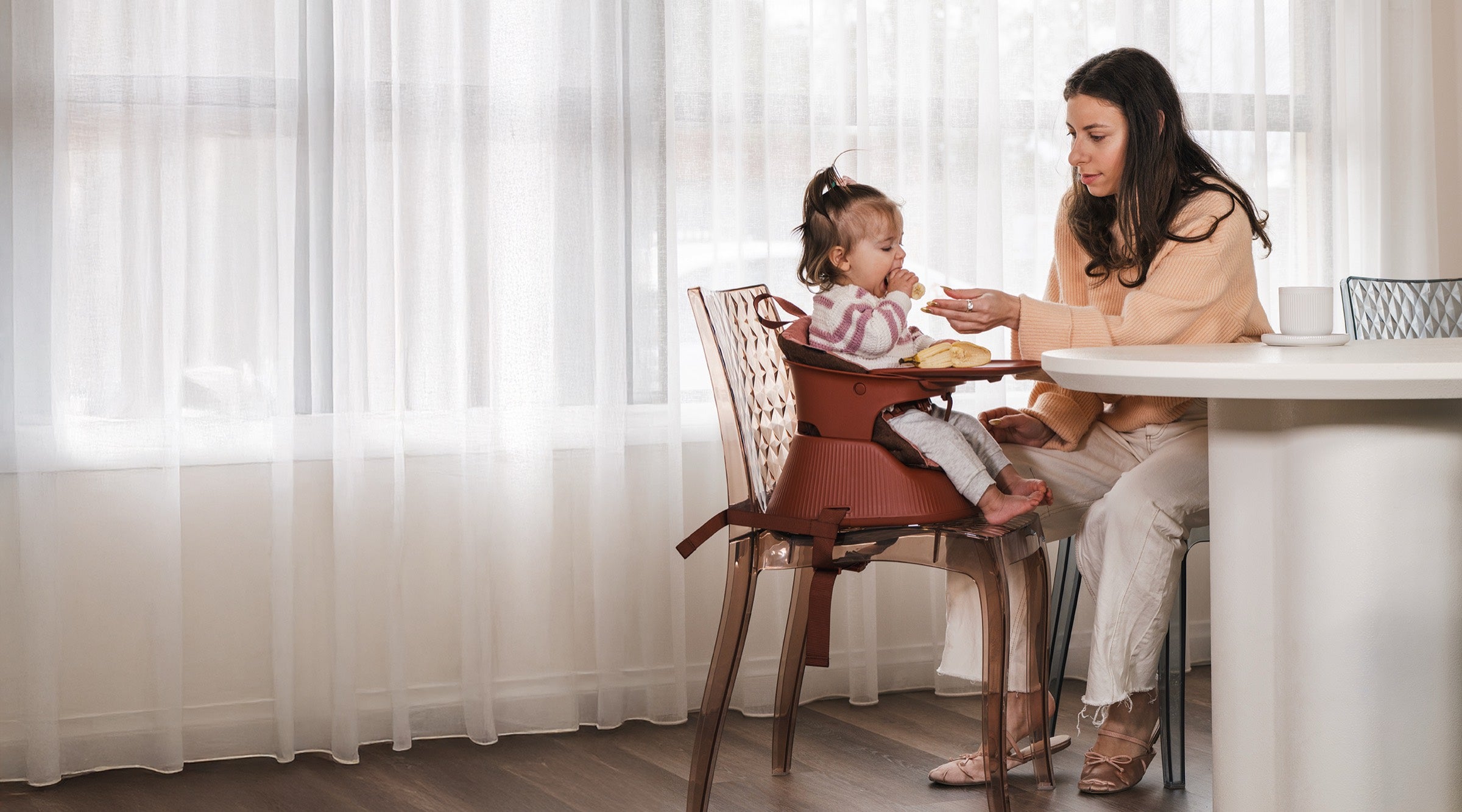 Mum feeding her toddler in the Hannie Portable High Chair at the dining table